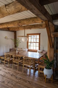 a wooden table and chairs in a room with exposed beams on the ceiling, along with potted plants