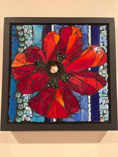 a red flower on a blue and white mosaic tile wall hanging in a black frame