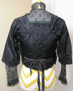 You are buying an authentic antique Victorain black blouse or waist. NOT a reproduction. This is from the late 1800s or early 1900s. It features a black satin lining with a black crepe overlay trim in lace and braid. The lining fastens in the front separate from the outside layer. It has black ties on the inside --not sure what they tied to. All fasterners are hook and eyes. The outside blouse also fastens in the front and top left with hooks and eyes. The closing placket has back lace.down the Fitted Vintage Black Blouse, Black Fitted Vintage Blouse, Vintage Black Top With Lace Trim, Fitted Black Vintage Victorian Dress, Vintage Black Blouse With Lace Trim, Black Vintage Victorian Dress, Fitted Black Blouse For Daywear, Victorian Fitted Blouse For Vintage Fashion, Black Victorian Dress With Historical Design