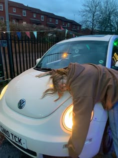 a woman leaning on the hood of a white car with her head in the window