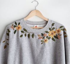 a gray sweater with flowers on it hanging on a hanger next to a white wall