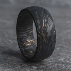 a black and gold wedding ring with an intricate design on the inside, sitting on a gray surface