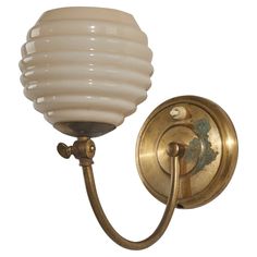 a wall light with a white glass shade on it's arm and an antique brass finish