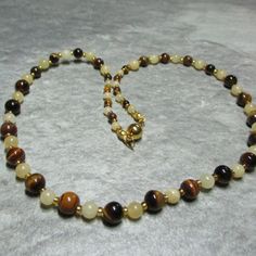 This necklace is made from Tigers Eye gemstone beads, in three sizes, alternate with 2 sizes of yellow Jasper separated by gold coloured glass seed beads. The Tigers Eye gemstones are 4mm at each end of the necklace changing to 6mm then 8mm at the centre, while the Jasper is 4mm at each end changing to 6mm. The magnetic clasp is gold plated stainless steel and the necklace comes with free matching earrings all enclosed within a cream fine velvet bag. Yellow Spiritual Beaded Necklace With Gemstone Beads, Gold Necklaces With Round Natural Stones, Gold Necklace With Round Natural Stone Beads, Gold Necklace With Round Natural Stones, Amber Beaded Necklaces With Spacer Beads As Gift, Gold Spiritual Gemstone Beads, Gold Spiritual Crystal Necklace With Polished Beads, Gold Natural Stones Round Beads, Gold Round Beads With Natural Stones