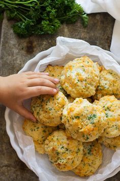 garlic cheddar biscuits in a white bowl with a hand reaching for the biscuit