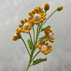 a crocheted yellow and white flower is shown in front of a gray background