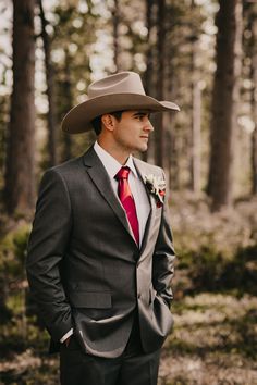 a man in a suit and red tie wearing a cowboy hat standing in the woods