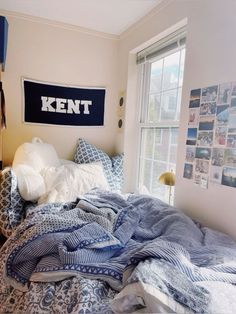 an unmade bed with blue and white comforter in a bedroom next to a window