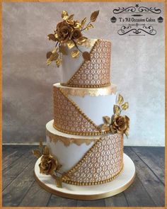 a three tiered cake with gold flowers on the top and bottom, sitting on a wooden table