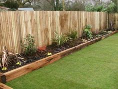 a wooden fence is next to a grassy area with flowers and plants in the middle