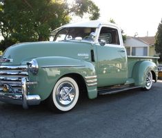 an old green truck is parked on the street