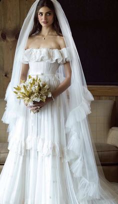 a woman in a white wedding dress with a veil on her head and flowers in her hand