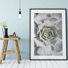 a large white flower in a frame on the wall next to a stool and table