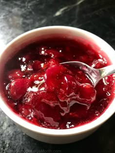 a white bowl filled with cherries sitting on top of a black counter next to a silver spoon