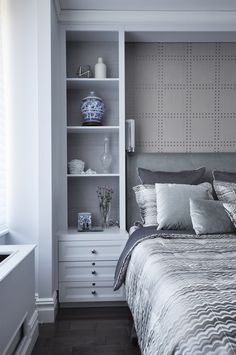 a bed sitting in a bedroom next to a white shelf filled with vases and flowers