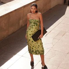 a woman in a yellow dress is walking down the street with her purse on her shoulder