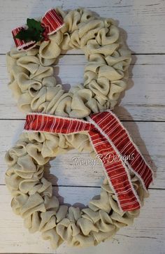 a wreath made out of burlocks and red ribbon on a white wooden background