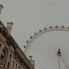 a large ferris wheel sitting next to a tall building on a cloudy day in front of a gray sky