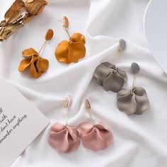 three pairs of flower shaped earrings sitting on top of a white cloth next to a card