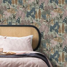 a bed sitting next to a wall covered in pink and green wallpaper with trees on it