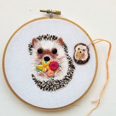 a hedgehog with flowers in it's mouth next to a needle and thread