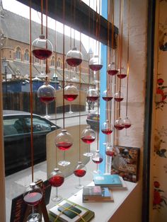 wine glasses are hanging from the ceiling in front of a window with books and magazines on it