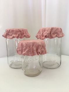 three glass jars with ruffles on them sitting on a white tablecloth covered surface