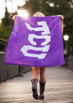 a woman walking down a wooden walkway holding a purple flag with the word go on it