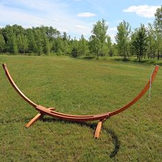 a wooden hammock sitting in the middle of a grassy field next to trees