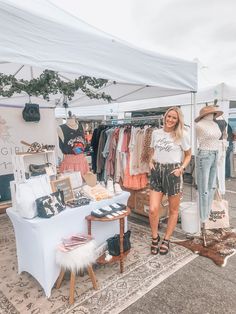 a woman standing in front of a tent with clothes on display and other items for sale