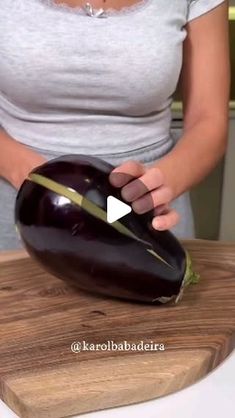 a woman holding an eggplant on top of a wooden cutting board