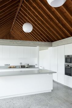 an empty kitchen with white cabinets and counter tops, along with hanging lights above the island