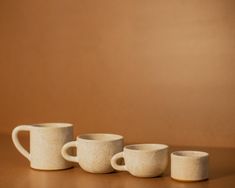 three white coffee mugs lined up on a brown table with one cup in the middle