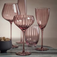 pink wine glasses are lined up on a table with nuts in a bowl next to them