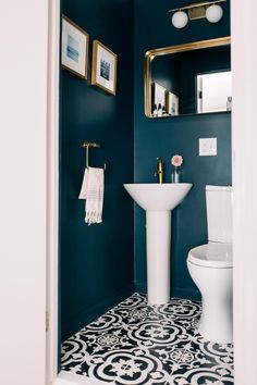 a white toilet sitting next to a sink in a bathroom under a mirror and framed pictures on the wall