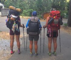 three people with backpacks and hiking poles are standing on the side of the road