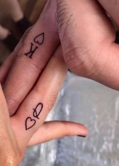 two people holding hands with tattoos on their fingers and one has the word love written on it