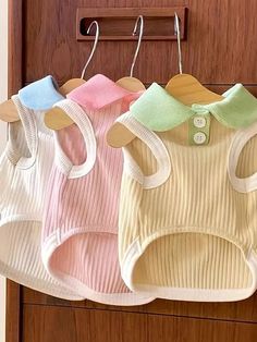 three baby vests hanging on a wooden door