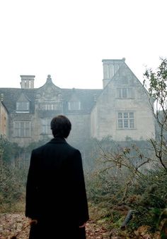 a man standing in front of a large building with lots of trees and leaves on the ground