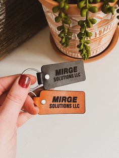 a person holding two keychains in front of a potted plant