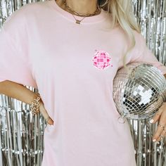 a woman wearing a pink t - shirt holding a disco ball in front of a silver background