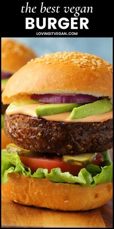 two hamburgers with lettuce, tomato and pickles on a cutting board