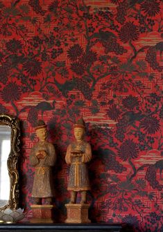 two statues are standing in front of a red wall