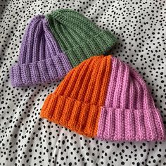 two knitted hats laying on top of a polka dot bed sheet, one is green and the other is pink