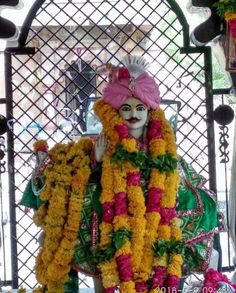 a man dressed up as a person with flowers around his neck and head, standing in front of a gate