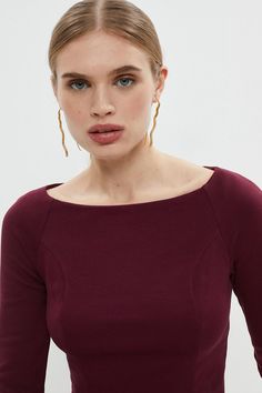 a woman in a maroon top is posing for the camera with her hands on her hips