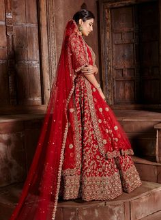 a woman in a red and gold bridal gown standing on steps with her arms around her neck