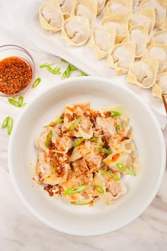 a white plate topped with dumplings next to a bowl of sauce and seasoning