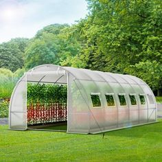 a small greenhouse in the middle of a grassy area with trees and bushes behind it