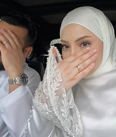 a woman covering her face while sitting in a car next to a man wearing a suit and tie